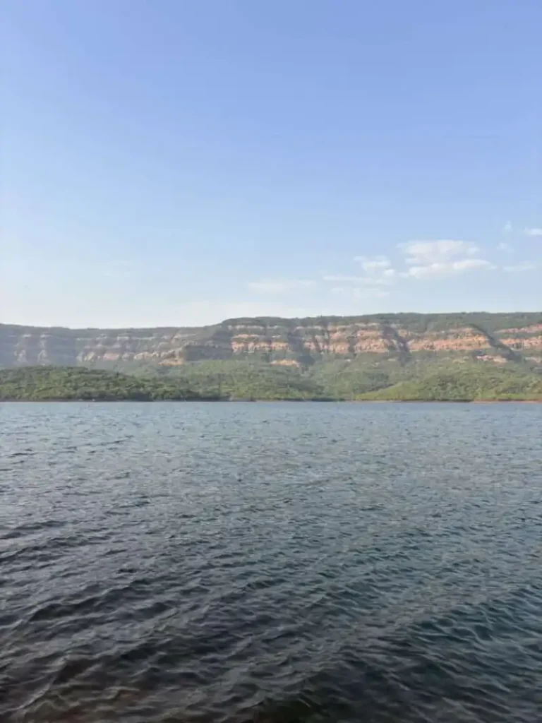Peaceful view of Ozarde Backwaters in Koyna with calm water, green hills, and cloudy skies, creating a serene natural setting near Koynanagar.