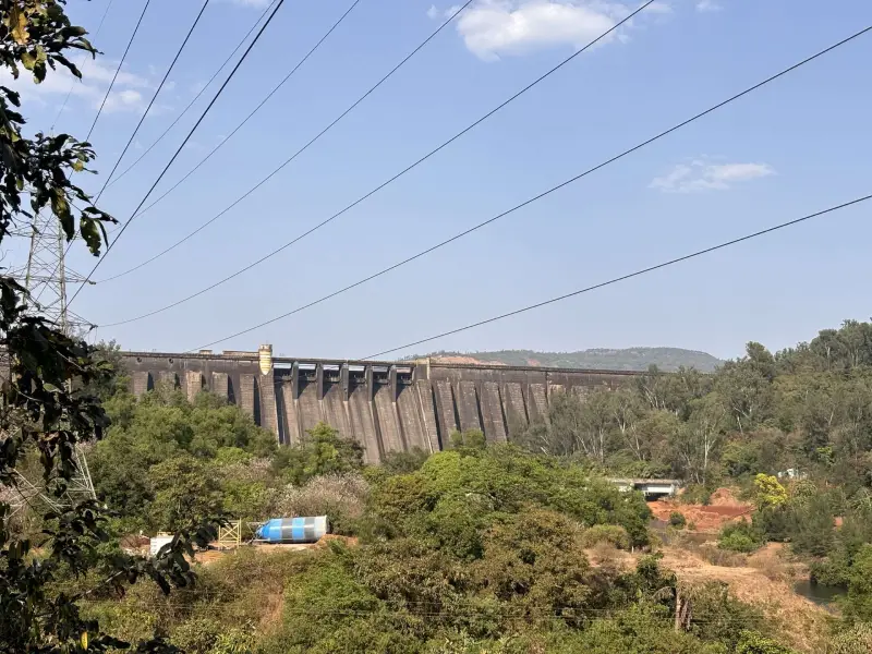 Panoramic view of Koyna Dam surrounded by lush green hills, with calm reservoir waters reflecting the overcast sky in Maharashtra's Western Ghats.